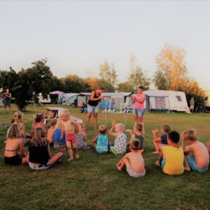 Een groep kinderen zit op het gras van Minicamping Falkenborg.
